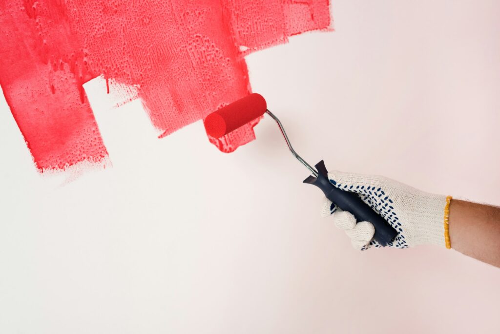 cropped shot of man in protective glove painting wall in red by paint roller